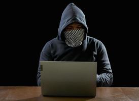 Hacker spy man one person in black hoodie sitting on a table looking computer laptop used login password attack security to circulate data digital in internet network system, night dark background. photo