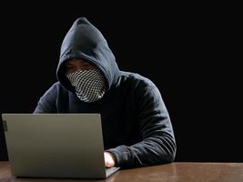 Hacker spy man one person in black hoodie sitting on a table looking computer laptop used login password attack security to circulate data digital in internet network system, night dark background. photo