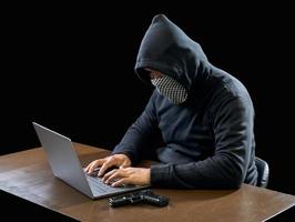 Hacker spy man one person in black hoodie sitting on a table looking computer laptop used login password attack security to circulate data digital in internet network system, night dark background. photo