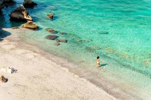 Aerial view tourist woman figure stand in clear turquoise water in persian gulf Mirellas island sandy white beach. Oman coastline paradise. Musandam. photo