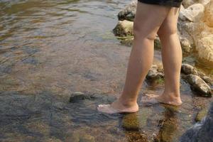 asiático mujer pisar descalzo caminar abajo un corriente con muy claro agua. junto a el arroyo, allí son muchos grande y pequeño rocas suave y selectivo enfocar. foto