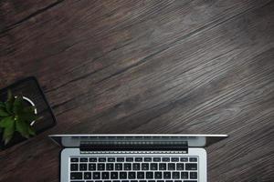 wooden office desk with laptop, blank notebook, cordless earphones and glasses, dark background, wooden background, Top view with copy space, empty space. photo