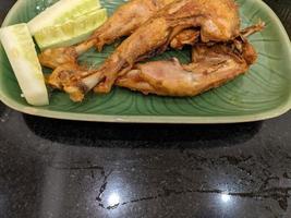 Fried Chicken with cucumber slice with green plate on the Indonesia traditional restaurant. The photo is suitable to use for food background, poster and food content.