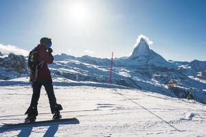 Young man snowboarding in Zermatt ski resort right next to the famous Matterhorn peak. Beautiful sunny day for snowboarding. Winter sports concept. photo