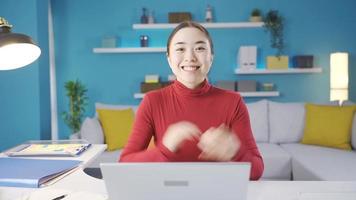 Young Asian woman looking at laptop alone at home satisfied with the view she sees on the screen and smiling looking at the camera, giving a positive gesture with her hand. video