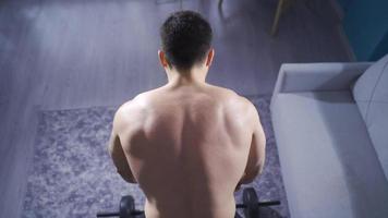 bodybuilder uomo Lavorando su a casa utilizzando pesi per indietro e braccio muscoli. muscolare bodybuilder Lavorando solo a casa per mantenere e rafforzare il suo fisico. video