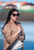 Portrait of stylish young woman with long hair, plump lips and sunglasses, dressed in beige coat photo