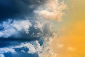 Dramatic blue thunderclouds on left, stunning yellow-golden fluffy clouds illuminated by rays of sun on right photo