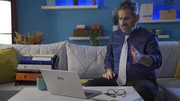 Mature businessman working from laptop at home receives distressing and disappointing news and becomes depressed and angry. video