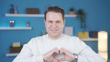 Cheerful and happy man at home making heart symbol. Adult man looking at camera at home making heart sign and smiling. video