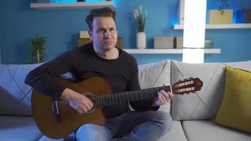 frustriert Mann Sitzung auf Sofa spielen seine Gitarre traurig und enttäuscht. frustriert Mann Sitzung auf Sofa spielen seine Gitarre traurig und enttäuscht. video