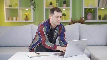 uomo sorridente a telecamera mentre Lavorando su il computer portatile. uomo giri per telecamera e sorrisi mentre Lavorando a partire dal il computer portatile a casa. video