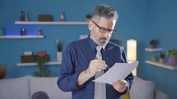 Mature businessman in suit working in home office, taking notes looking at documents and paperwork, taking off his glasses. video