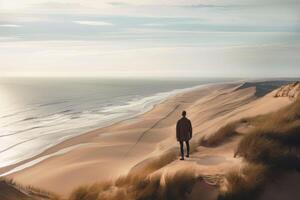 hombre en pie en parte superior de un grande arena duna, mirando fuera a través de un vasto paisaje hacia el Oceano en el costero región, ai generado foto