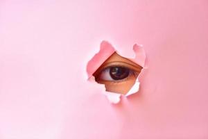 observando ojo de un bebé niña en el agujero de rosado papel. ojo debajo rosado papel. foto