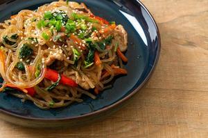 japchae or stir-fried Korean vermicelli noodles with vegetables and pork topped with white sesame photo