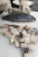 enfocado masculino cocinero en uniforme corte pescado filete en junta, cocinero cortes blanco tilapia pescado en cocina. foto