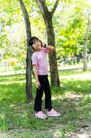 Portrait of child girl listens to music with modern headphones in park outdoors. Happy child enjoying rhythms in listening to music with headphones wireless photo