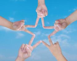 Child hands uniting their to make star shape with fingers, over blue sky background. Conceptual of teamwork. photo