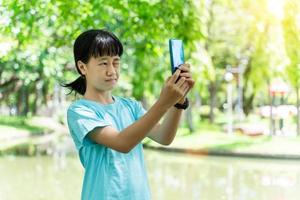 portrait of young asian child girl using mobile smartphone while in the park in warm spring day. photo