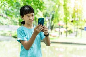 portrait of young asian child girl using mobile smartphone while in the park in warm spring day. photo