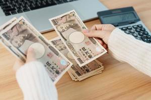 mano de mujer contando billetes de yen japonés con calculadora. dinero de mil yenes. Japón efectivo, impuestos, economía de recesión, inflación, inversión, finanzas, salarios y conceptos de pago foto