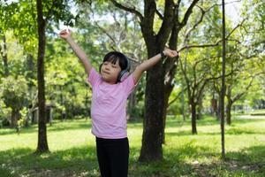 Portrait of child girl listens to music with modern headphones in park outdoors. Happy child enjoying rhythms in listening to music with headphones wireless photo