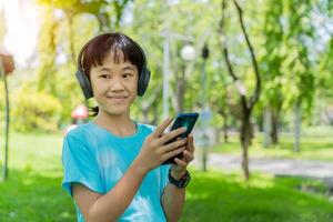 Pretty school girl with smartphone and listens to music with modern headphones wireless in park outdoors. photo
