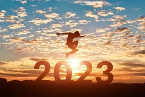 Silhouette of man jumping to Happy new year 2023 in sunset or sunrise background. photo