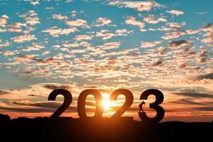 Silhouette of photographer taking photos in 2023 years at sunrise or sunset background. Idea for happy new year 2022.