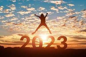 Silhouette of young woman jumping to Happy new year 2023 in sunset or sunrise background. photo