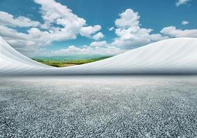 Asphalt ground and curved art building with green mountains, blue sky and white clouds background photo