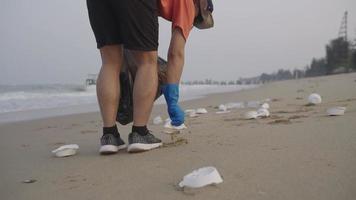 vicino su. volontari camminare e raccogliere su spazzatura su il spiaggia. addetto alle pulizie raccolta spazzatura su il nero sabbia spiaggia in bianca plastica borse. volontari pulizia il spiaggia. riordino su sciocchezze su il spiaggia video