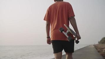 espalda ver.a hombre caminando llevar con un patineta relajante cerca el mar video
