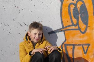 Boy teenager near the wall with funny graffiti. photo