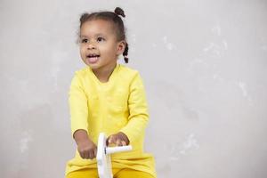 Little African American girl in yellow clothes shows tongue. Funny child. photo