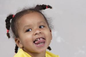 Little African American girl in yellow clothes shows tongue. Funny child. photo