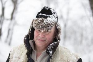 un mayor hombre en un invierno sombrero cubierto con nieve sonrisas y mira dentro el cámara. foto