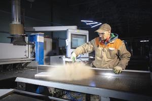 A furniture manufacturing worker at a cutting machine makes furniture parts. Furniture manufacturing. photo