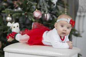 pequeño bebé a Navidad. tres meses de edad niña en contra el antecedentes de el Navidad árbol decoración. foto