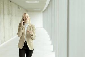 Businesswoman using mobile phone on modern office hallway photo