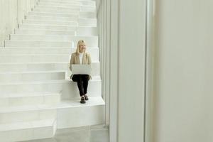 Businesswoman with laptop on modern office stairs photo