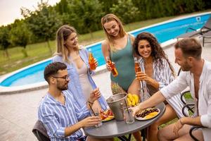 Group of young people cheering with cider by the pool in the garden photo