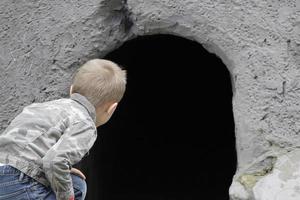 The child looks into the black hole of the cave. The concept of learning the unknown. Childish curiosity. photo