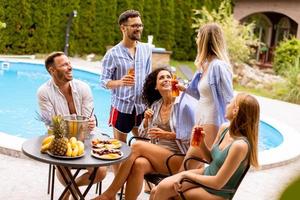 Group of young people cheering with cider by the pool in the garden photo