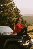 mujer joven relajándose en el capó de un vehículo de terreno en el campo foto