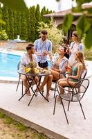 grupo de jóvenes animando con sidra junto a la piscina en el jardín foto