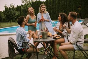 Group of young people cheering with cider by the pool in the garden photo