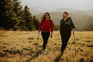 Smiling couple walking with backpacks over green hills photo