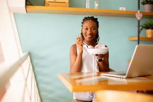 Young black woman having a healthy breakfast while working on laptop in the cafe photo